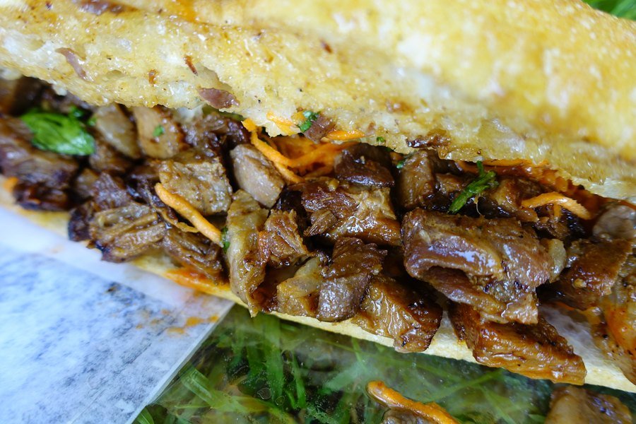 Close-up of a banh mi stuffed with caramelised pork, herbs and pickled carrot