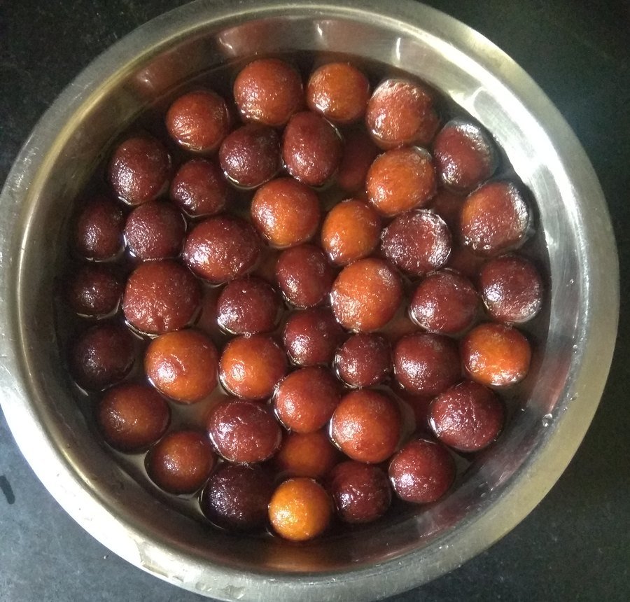 A steel bowl of gulab jamuns soaking in sugar syrup